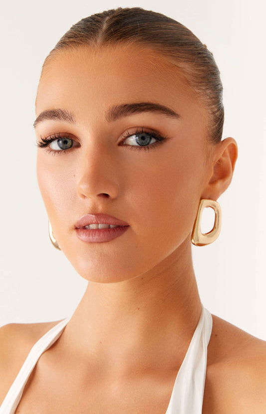 A woman wearing a golden earring from Peppermayo US accessories collection.